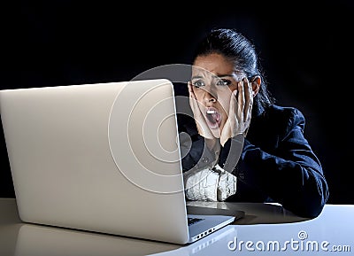 Woman working in darkness on laptop computer late at night surprised in shock and stress Stock Photo