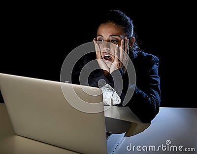 Woman working in darkness on laptop computer late at night surprised in shock and stress Stock Photo