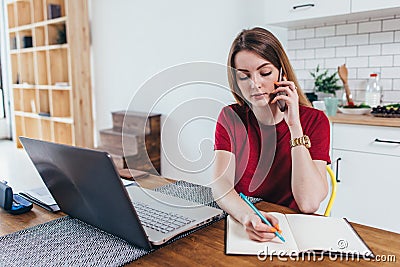 Woman working at home write notes while talking on phone Stock Photo