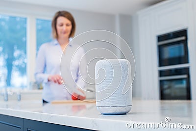 Woman Working In Kitchen With Smart Speaker In Foreground Stock Photo