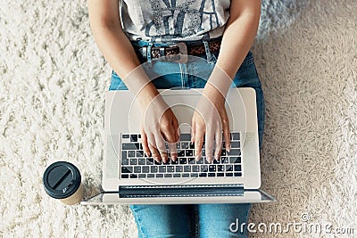 Woman working on a laptop. Female using a laptop sitting on floor, searching web, browsing information, having workplace at home. Stock Photo