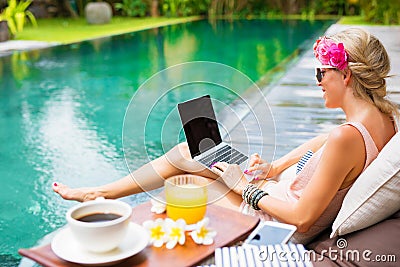 Woman working on laptop while sitting by the pool Stock Photo