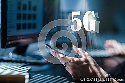 woman working in an office or home office using 5G technology - hand holding smartphone, laptop and monitor in the background Stock Photo