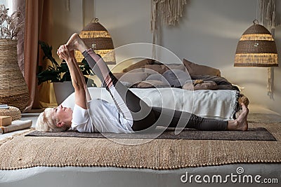 Woman working out, warming up using yogic belt, lying in yoga Supta Padangushthasana, One Leg Lift exercise Stock Photo