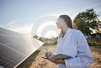 Woman working in solar energy, writing research on solar panels and studying sustainability of clean energy in summer Stock Photo