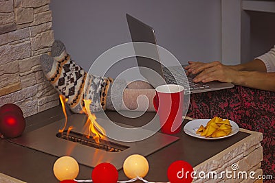 A woman works from home on a laptop in a comfortable environment, next to an open eco-friendly biofuel fireplace. No Stock Photo