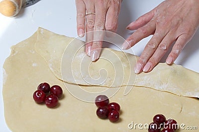 A woman wraps cherries and blueberries in a dough that are lying on a rolled dough. Cooking dumplings Stock Photo