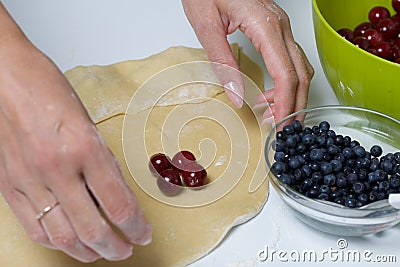 A woman wraps cherries and blueberries in a dough that are lying on a rolled dough. Cooking dumplings Stock Photo