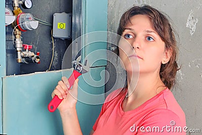 A woman with a wrench in her hand pondered next to the water pipes, close-up. Repair of sewer apartment, installation and Stock Photo