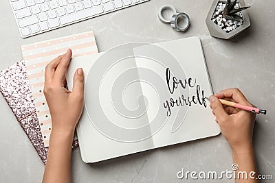 Woman writing LOVE YOURSELF in journal on grey table Stock Photo