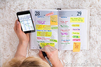 Woman Writing Note In Diary Using Mobilephone Stock Photo