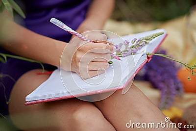 Woman writing in notebook with bouquet of wildflowers - lupines. Closeness to nature, self-discovery concept. Close up Stock Photo