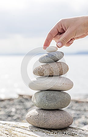Woman& x27;s hand balancing a stack of stones on a driftwood beach log. Stock Photo