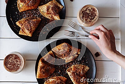 The woman& x27;s hand decorates the table with fork, knives, and pancakes. Black plate, white table. From the above Stock Photo