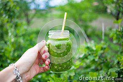 woman& x27;s hand holding jar with green cold-pressed juice, vegetable garden background. Healthy eating, detoxing, juicing, body Stock Photo