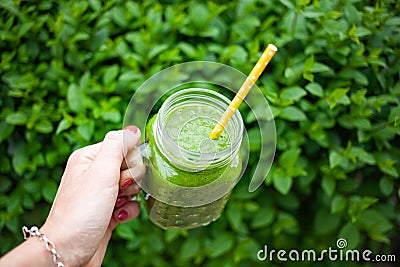 woman& x27;s hand holding jar with green cold-pressed juice, vegetable garden background. Healthy eating, detoxing, juicing, body Stock Photo