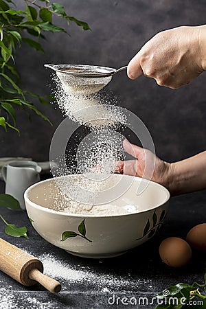 Woman& x27;s hand sifting flour through sieve. Selective focus. Baking, cooking, pastry abstract concept. Dark background Stock Photo