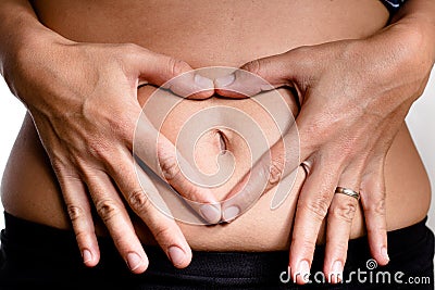 Woman& x27;s hands making a heart shaped symbol over the belly button symbolizing pregnanc Stock Photo