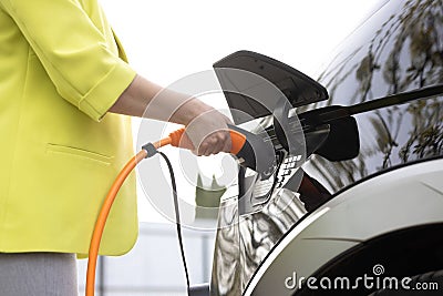Woman& x27;s hands unplugging her electric automobile and closing the hatch in front of her home. Female unplugging the Stock Photo