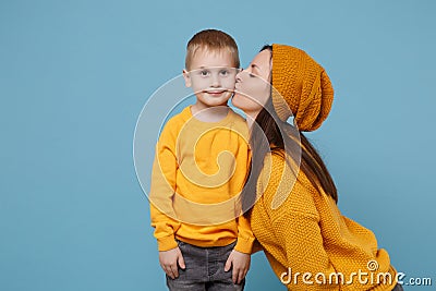 Woman in yellow clothes kissing kiss cheek cute child baby boy 4-5 years old. Mommy little kid son isolated on blue Stock Photo