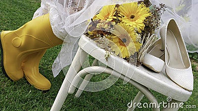 Woman in yellow gumboots and white spring dress next to a wooden chair and bouquet of yellow Gerbera daisy Stock Photo