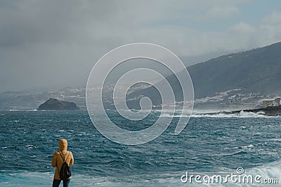 Woman with yellow jacket looking the fierce ocean Stock Photo