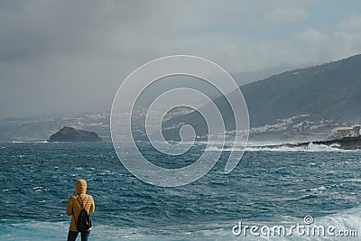 Woman with yellow jacket looking the fierce ocean and waiting the storm Stock Photo