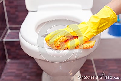 Woman in yellow rubber gloves cleaning toilet seat with orange cloth. Bathroom and toilet hygiene. Stock Photo