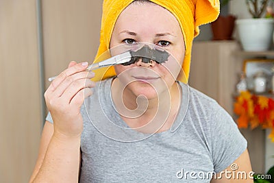 A woman in a yellow towel on her head and in a gray T-shirt applies a mask of blue clay to her face with a brush Stock Photo