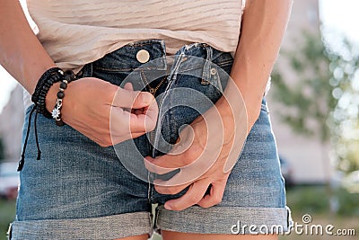 Woman zips up denim shorts, outdoors, on a blurred background. Stock Photo