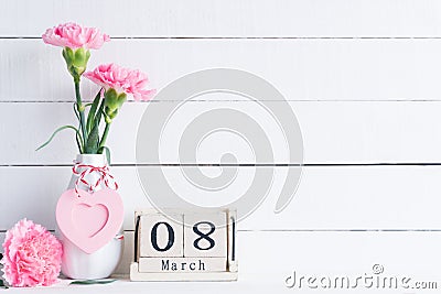 Womans day concept. Pink carnation flower in vase and red heart with March 8 text on wooden block calendar on white wooden Stock Photo