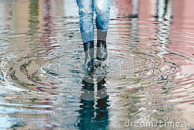 Womans feet with black rubber boots and blue jeans standing in a puddle of water after rain on a city street. Front view Stock Photo