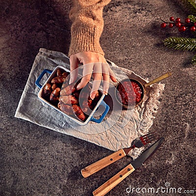 Womans Hand Reaches For Dish Of Traditional Christmas Pigs In Blankets On Table Set For Meal Stock Photo