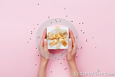 Womans hands holding gift or present box decorated confetti on pink pastel table top view. Flat lay composition for birthday. Stock Photo