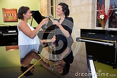 Women in cocktail dress near piano drinking champagne Stock Photo