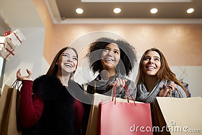 Women of diverse ethnicity with shopping bags posing in mall on sale. Portrait of three smiling multiracial girls look Stock Photo