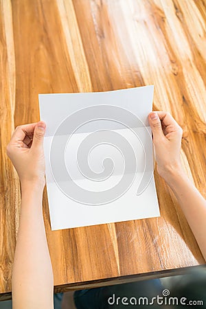 Women hand hold Trifold white template paper on wood texture . Stock Photo