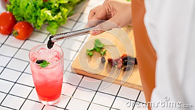 Women hands prepairing mocktail by putting sweet mulberry into a glass with an iced pink color drink Stock Photo