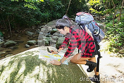 Women hiker with backpack checks map to find directions in wilderness area at waterfalls and forest. Stock Photo