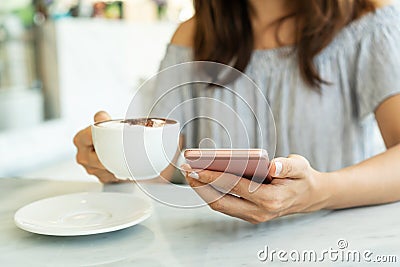 Women hold a cup of coffee while using mobile phone Stock Photo