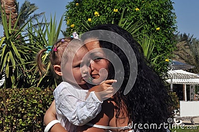 A woman with long, black curly hair embraces her daughter on a sunny day. Stock Photo