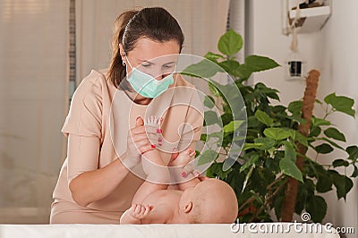 A woman makes a massage to a newborn in a medical mask. COVID 19 and baby care concept. Massage, colic, teething children Stock Photo