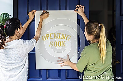 Women putting opening soon sign on a front door Stock Photo