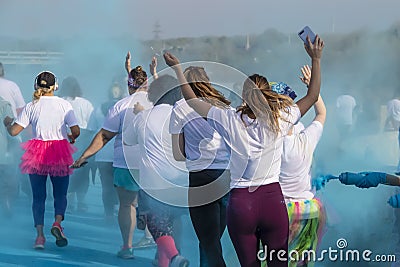 Women run in a holi color run race with arms raised with blue powder swirling around them - unrecognizable people Editorial Stock Photo