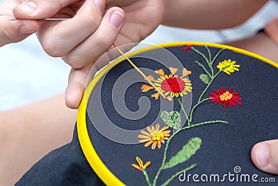 Women`s hand embroidery in a hoop, a woman embroider a pattern on dark material. Close-up. The concept of needlework, hobby, Stock Photo