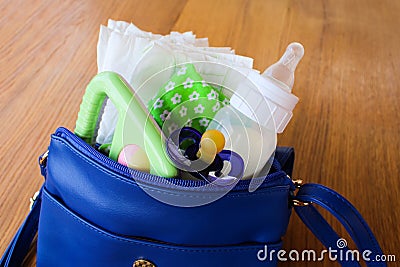 Women's handbag with items to care for the child: bottle of milk, disposable diapers, rattle, pacifier and baby clothes. Stock Photo