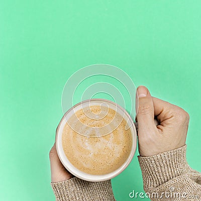 Women`s hands with cup of coffee above trend color mint paper surface. Sweet hot fragrant Stock Photo