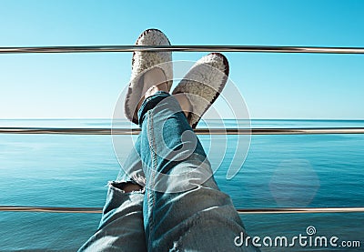 Women`s legs in torn jeans and white sheep fur slippers lying on the crossbar of the balcony Stock Photo