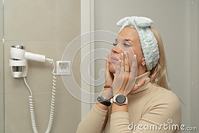 Women's morning preparations for work. A girl applies cream to her face in front of a mirror in the bathroom Stock Photo