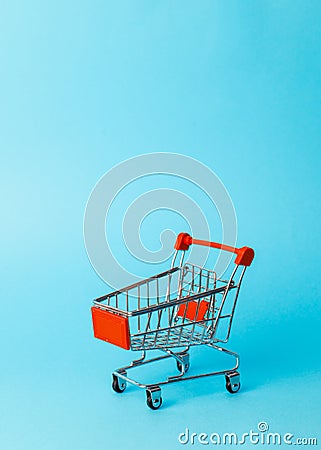 Women`s shopping: an empty miniature red trolley from a supermarket on a blue background. Stock Photo